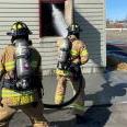 Two firefighters practice fire suppression from the exterior.